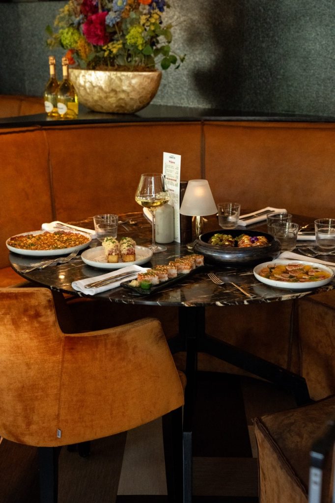 Tafel vol gerechten en sushi in een cognackleurige zitbank bij Brasserie Pastis