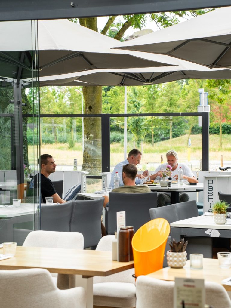 Gasten lunchen aan tafel op het terras van Brasserie Pastis, onder de parasols