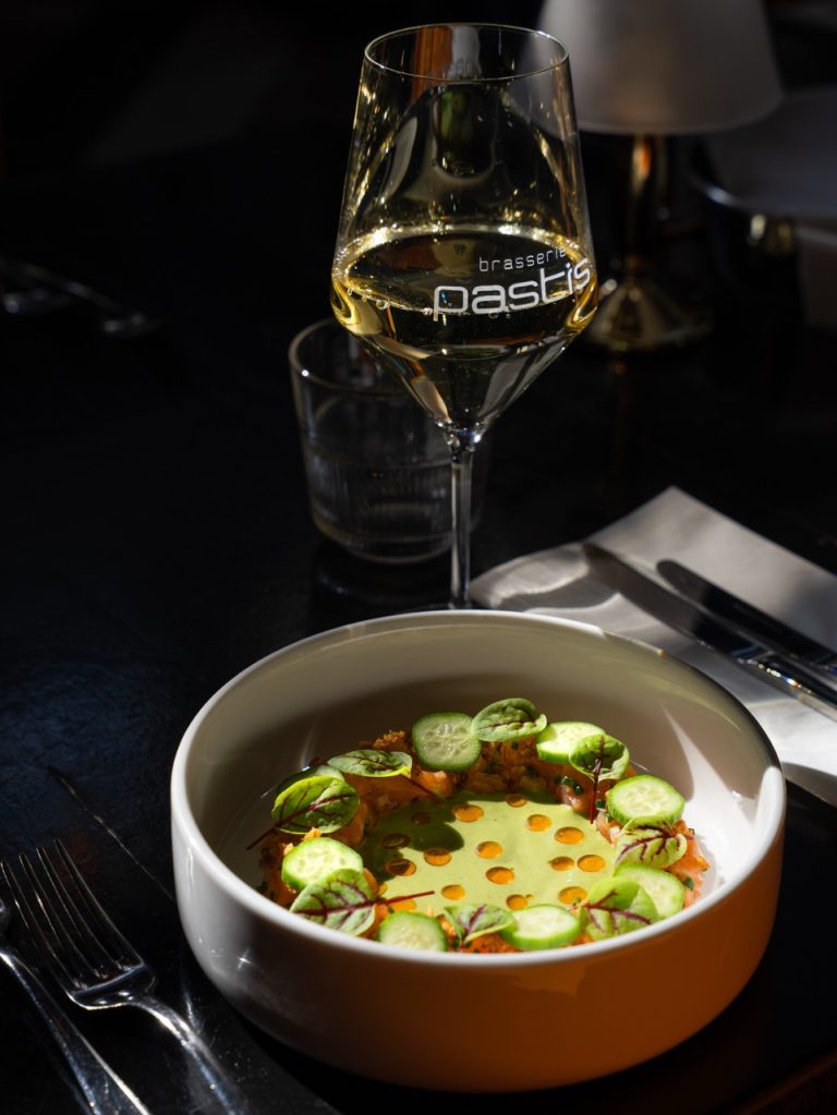Gerecht met groene saus en komkommer in een witte kom, naast een glas witte wijn met het Pastis-logo