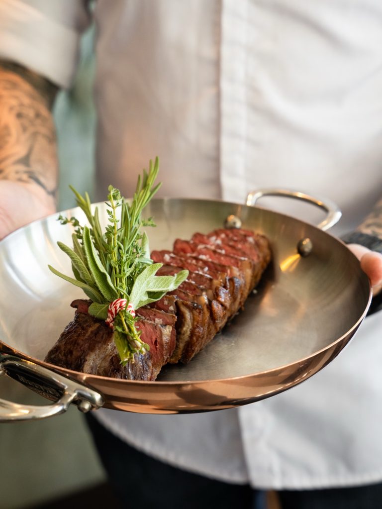 Kok draagt een koperen pan met gegrilde steak en verse rozemarijn