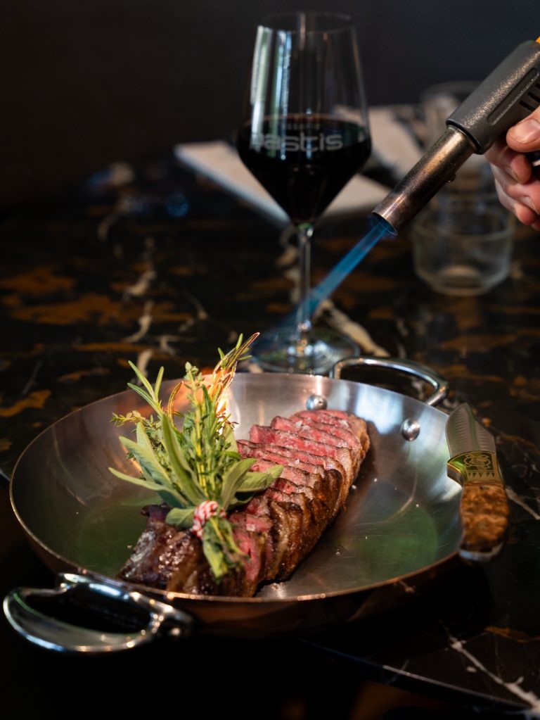 Gegrilde steak in een koperen pan naast een glas rode wijn